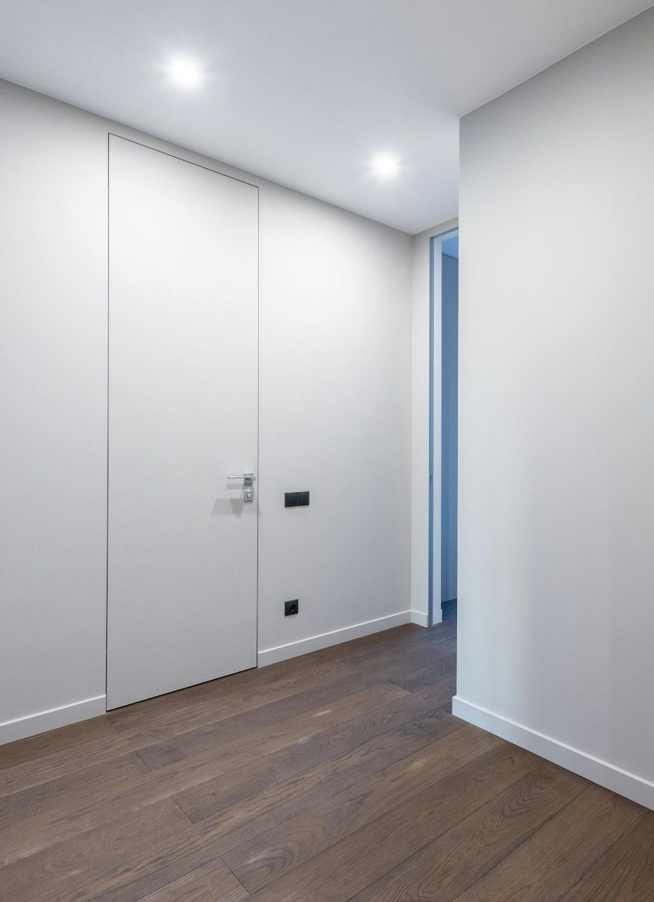 Hallway with dark wood flooring, white walls, recessed lighting, and a hidden door with a handle.