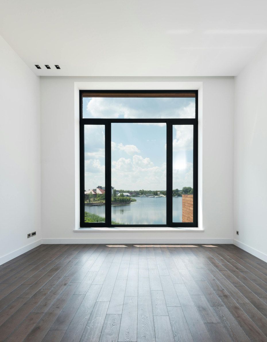 Empty room with dark wood floor, large window overlooking a body of water, white walls, and black window trim.