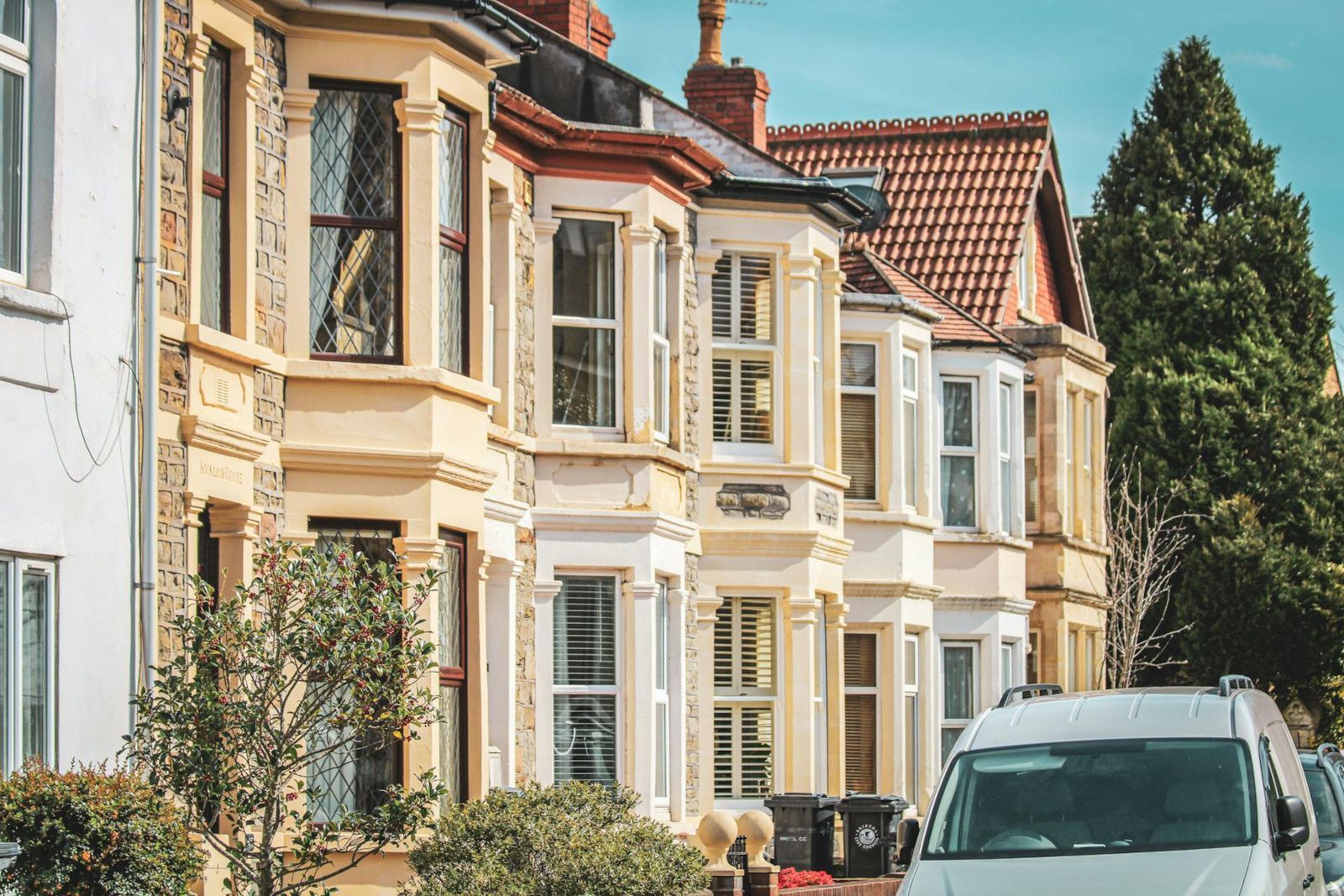 A white van is parked in front of a row of houses.