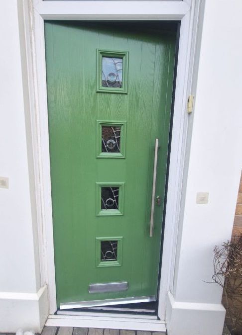 A green front door with four square windows and a stainless steel handle.