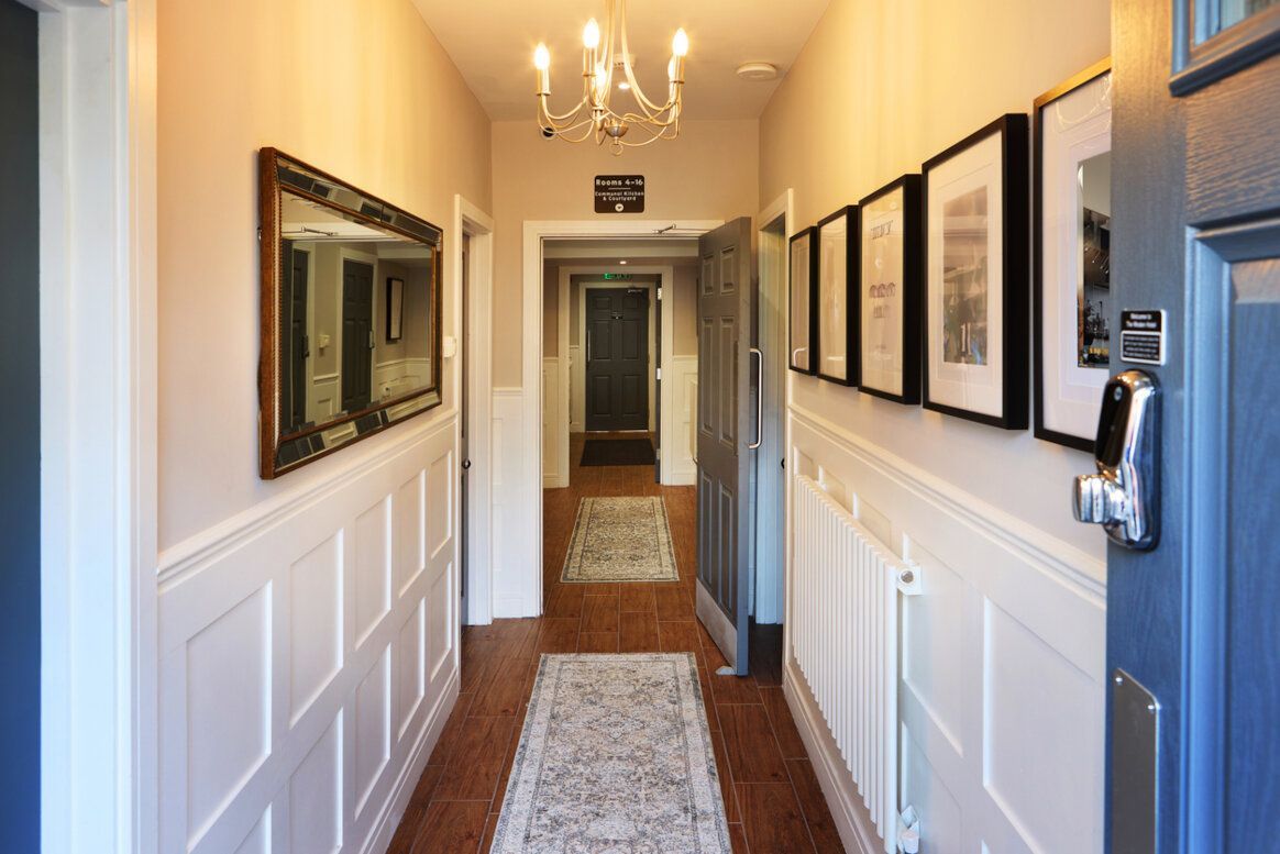 Hallway with white wainscoting, framed art, a mirror, and a chandelier; door open to the right.