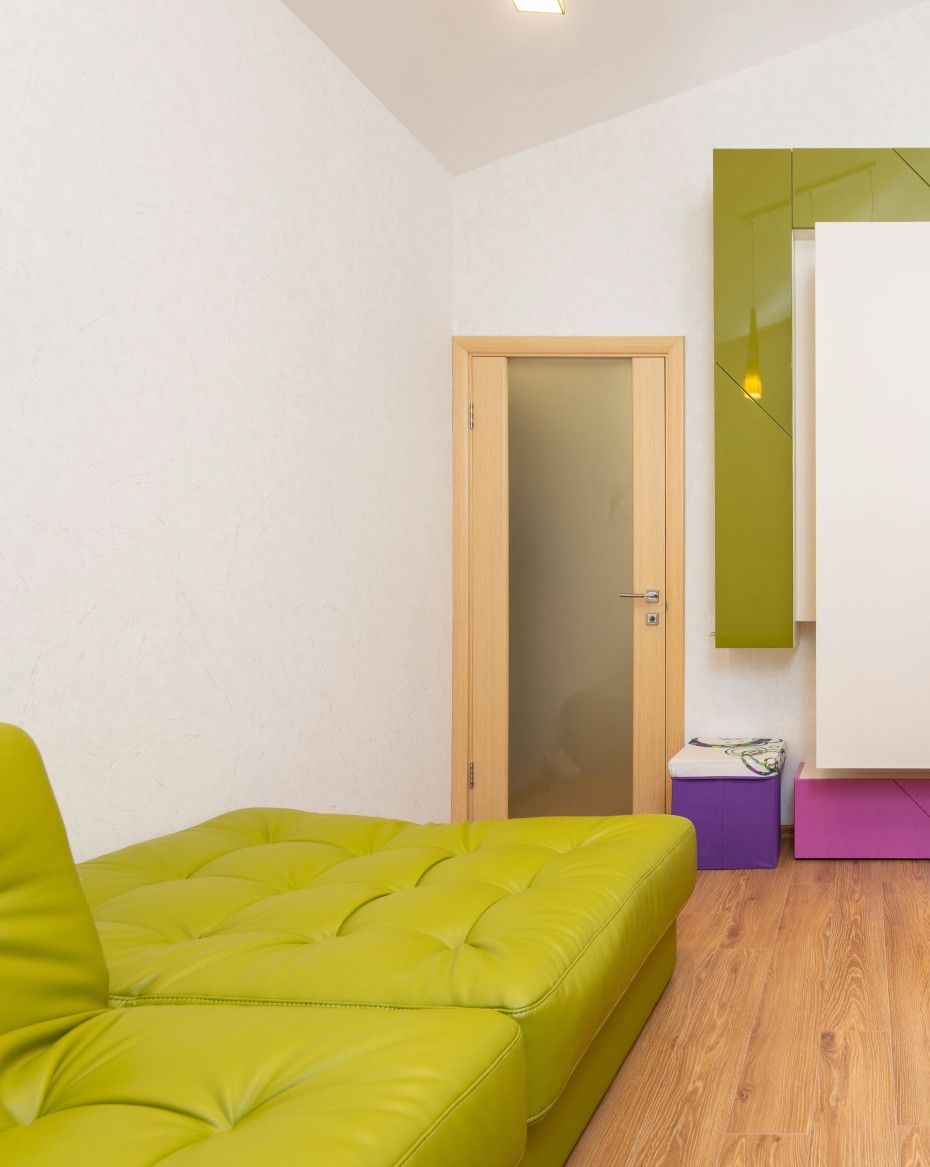 A living room with a green couch and a purple ottoman.