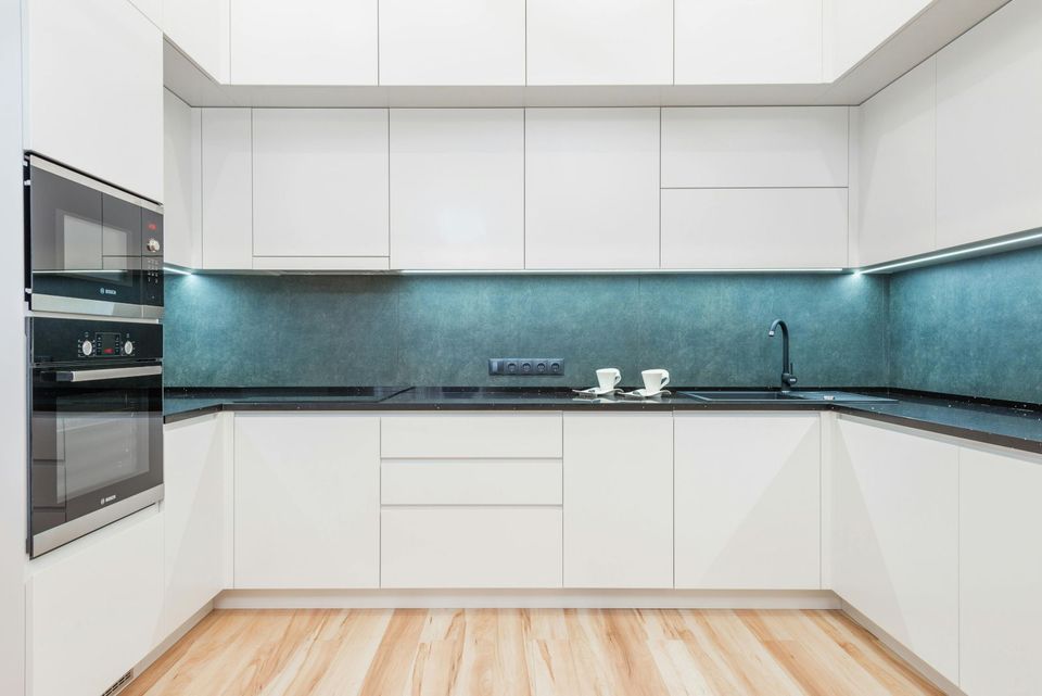 A modern kitchen with white cabinets and a wooden floor.