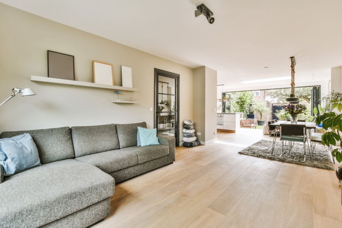 Gray sectional sofa in a light-floored living room with a shelf, door, and dining area visible.