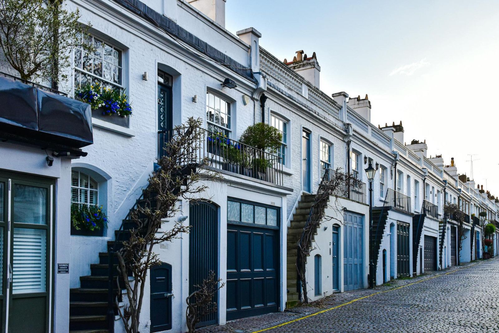 A row of white houses with stairs leading up to them on a cobblestone street.