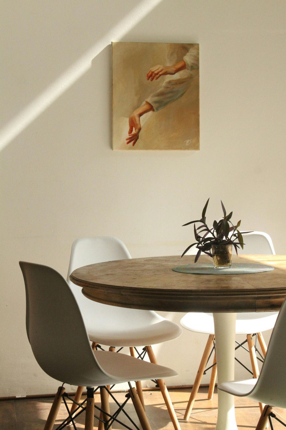 A dining room with a round wooden table, white chairs, and a painting of a hand.