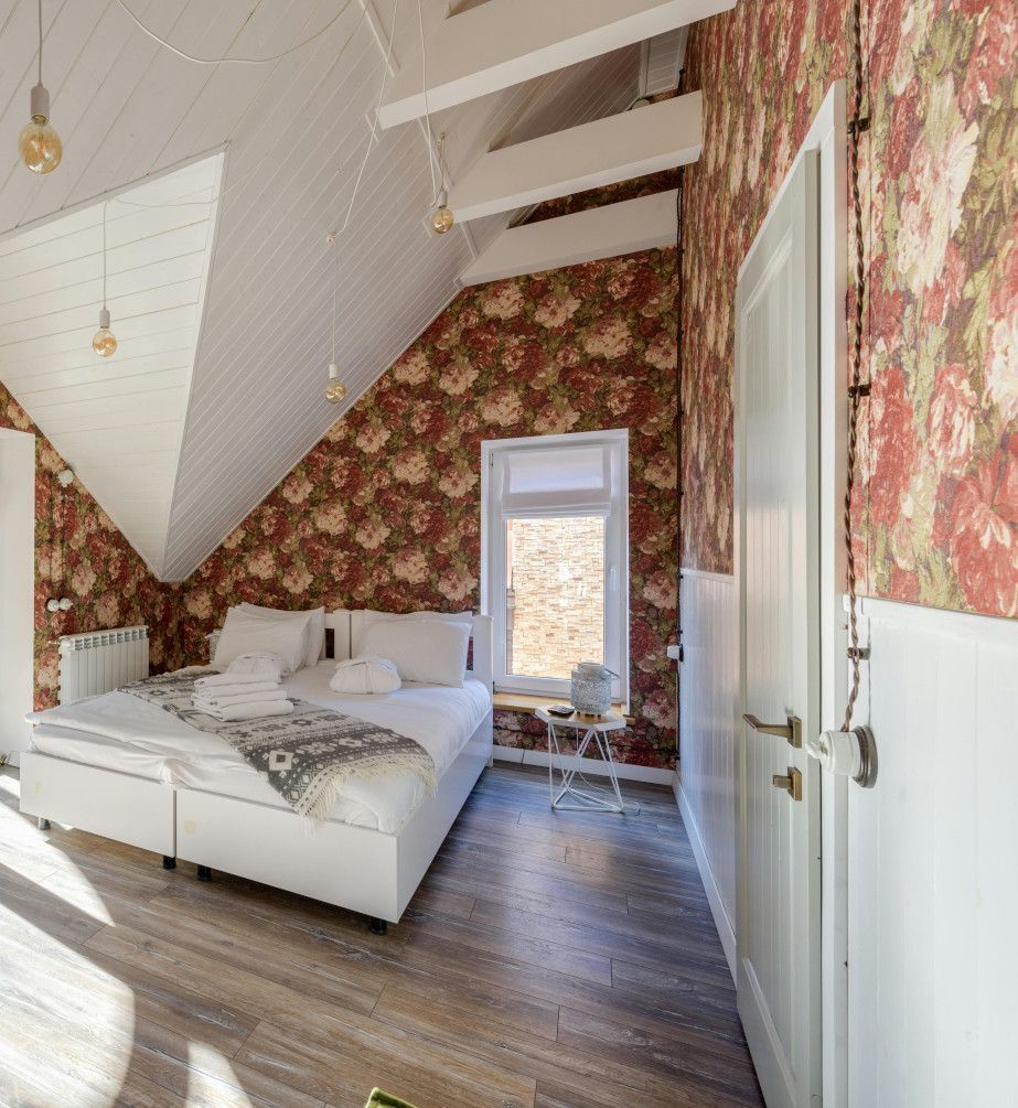 A bedroom with a bed and a window with floral wallpaper on the walls.