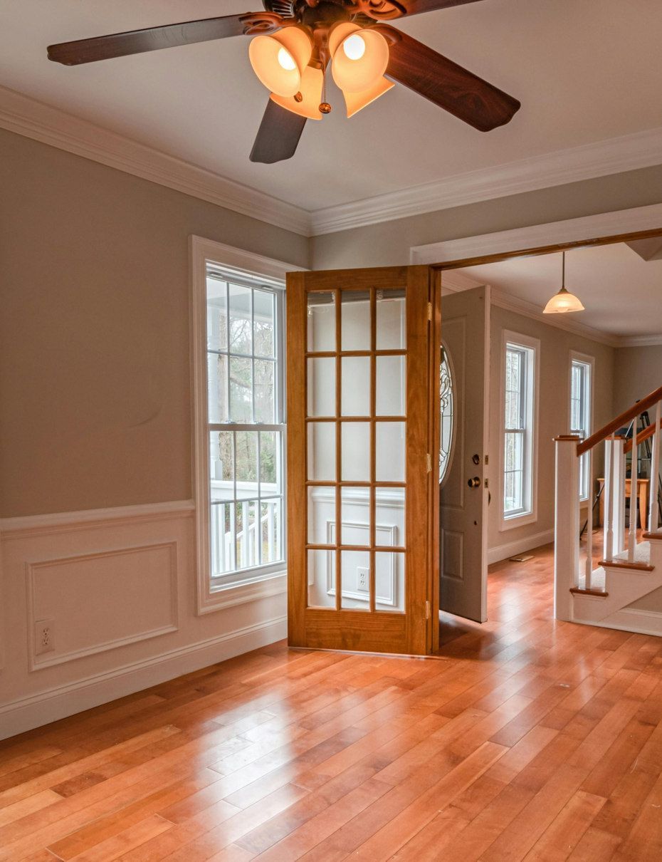 A bright, empty room with wooden floors, tan walls, and a wooden door with glass panes opening into another room.