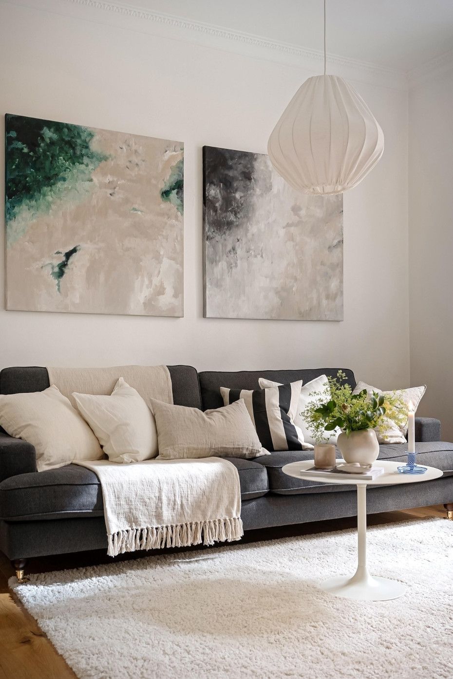 A living room with a couch , coffee table , and two paintings on the wall.