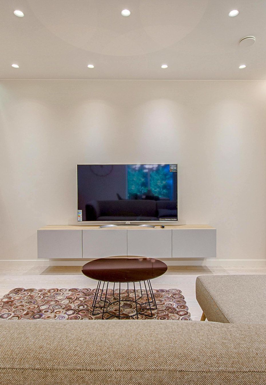 Living room with a mounted TV above a floating console, with a coffee table and patterned rug.