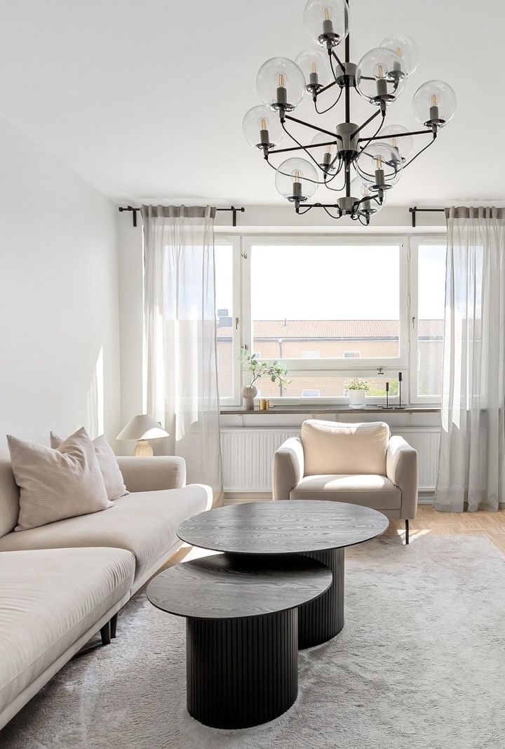 A living room with a couch , chair , coffee tables and a chandelier.