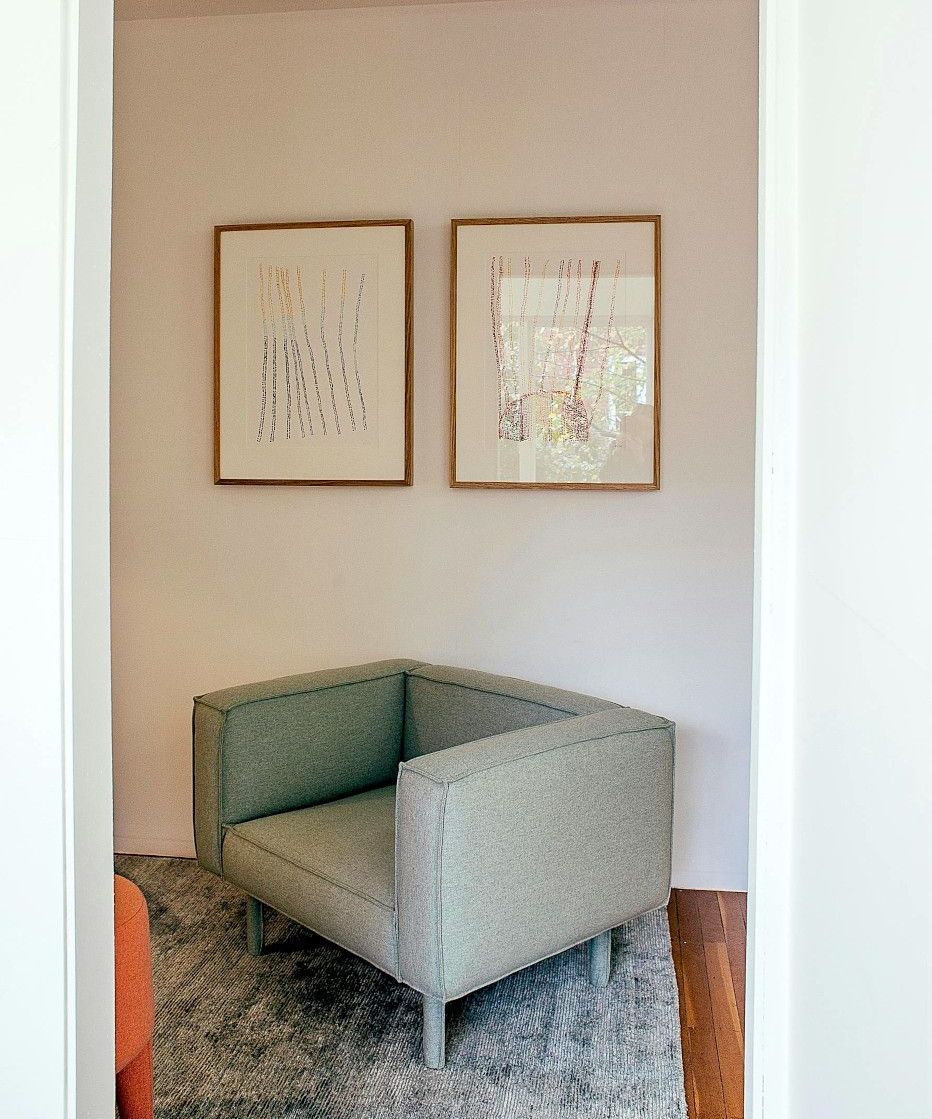 A small, mint-green armchair sits in a doorway alcove, under two framed artworks. The floor is covered with a gray rug.