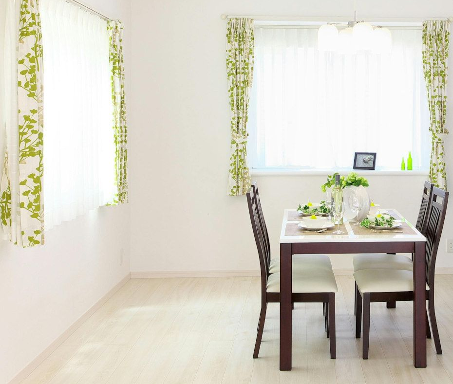 Dining room with table, chairs, windows with green curtains, and floral table setting.