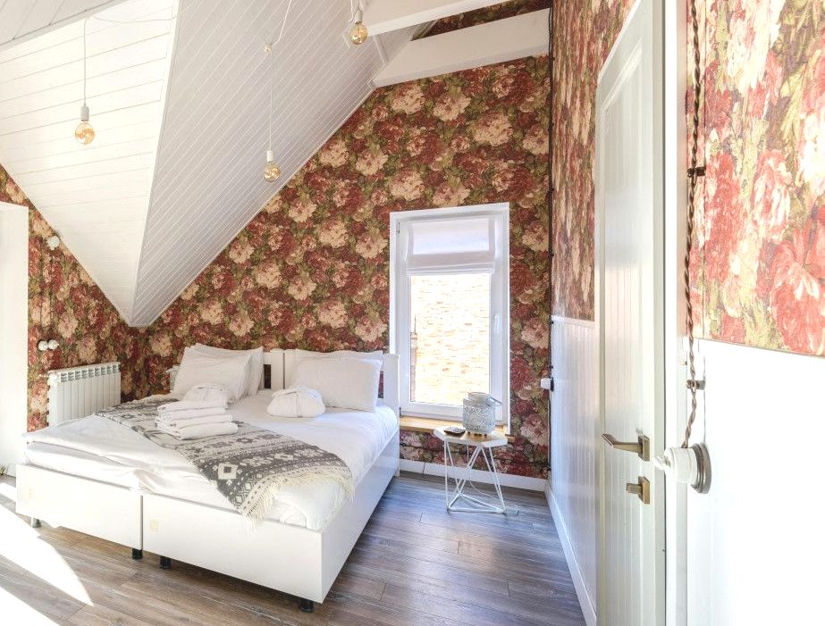 A bedroom with a bed and a window with floral wallpaper on the walls.