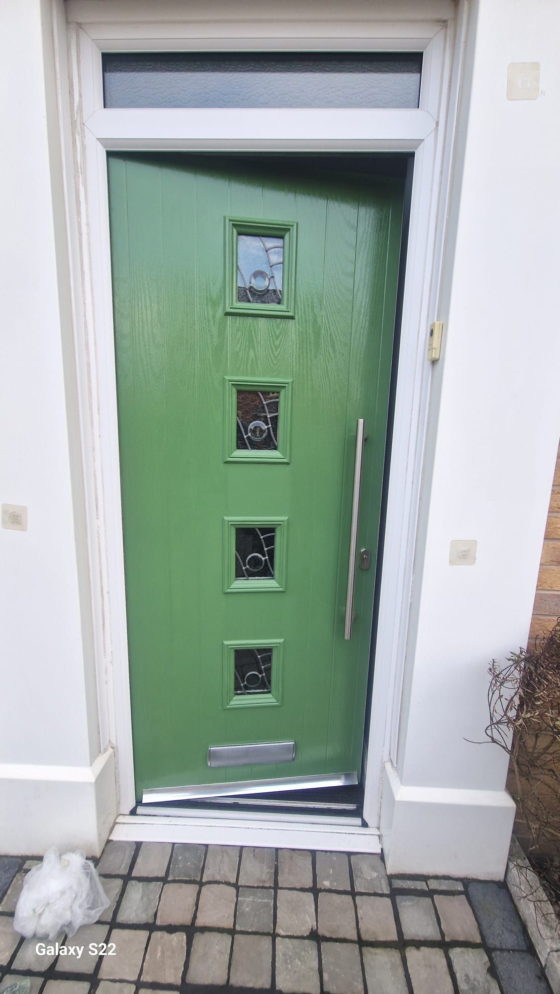 Green front door with small glass panels, vertical handle, and white trim.