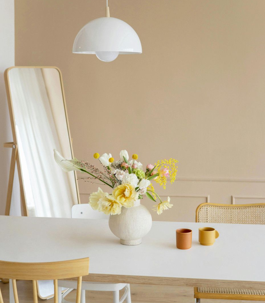 Dining room with white table, flowers, mirror, and white pendant light.
