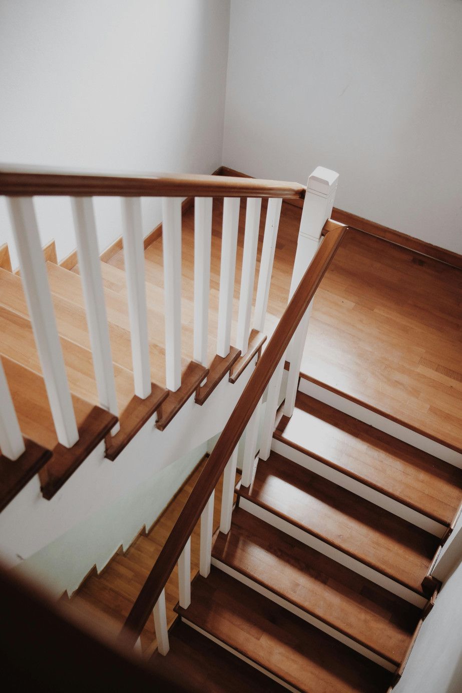 Wooden staircase with white balusters and brown handrails, viewed from above.