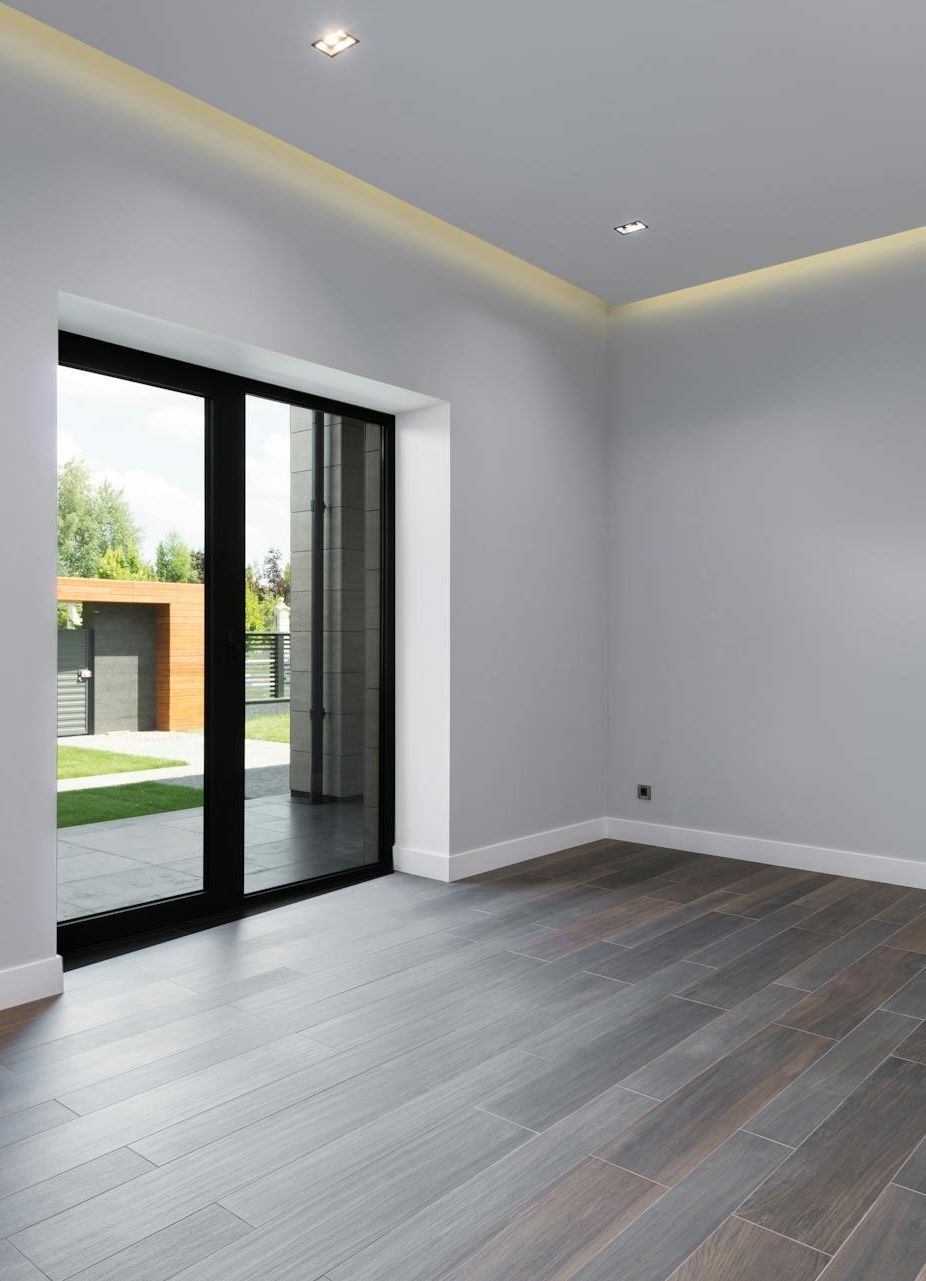 Empty room with dark wood floors, sliding glass door, and light gray walls.