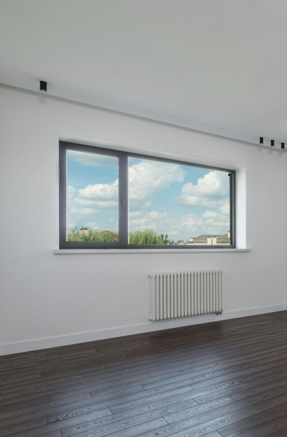 Room with a large window looking out at a blue sky. Radiator on the wall.