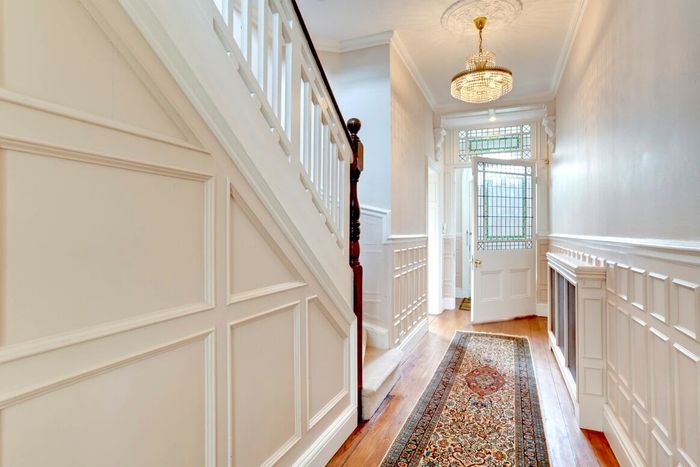 Hallway with white paneled walls, staircase, open door with stained glass, rug.