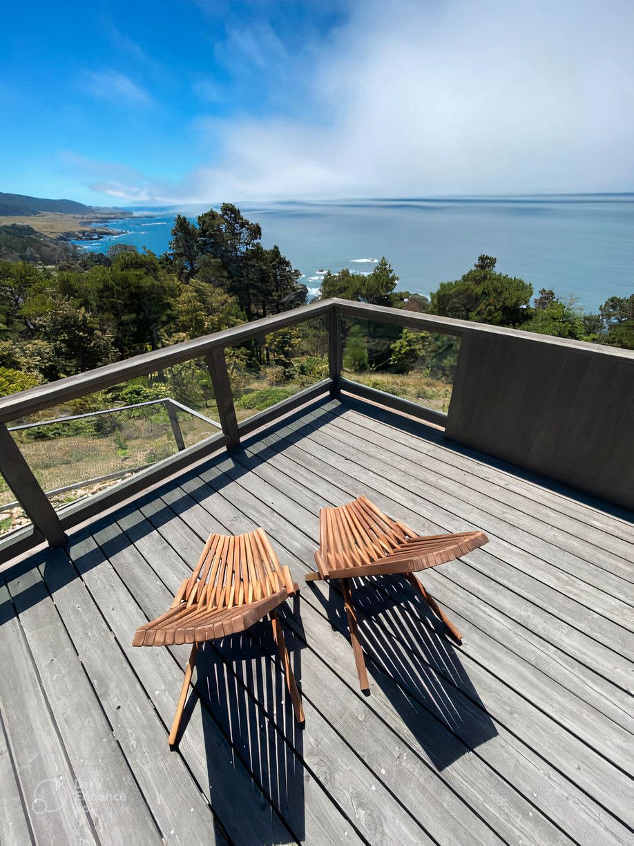 Two chairs are sitting on a wooden deck overlooking the ocean.