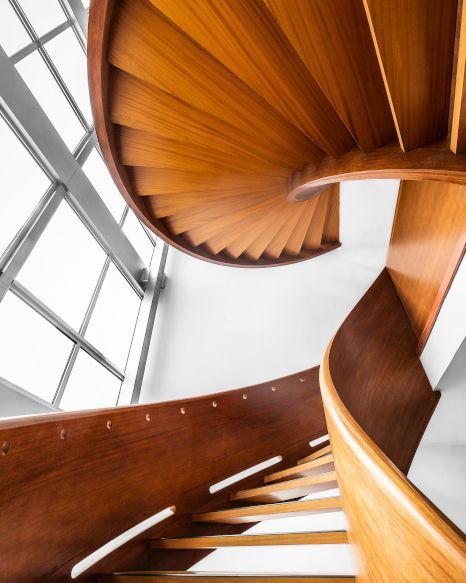 Looking up at a wooden spiral staircase in a building. Expertly varnished by Rose Decor in Preston, UK.