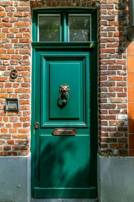 A painted green front door with a lion knocker is on a brick building. Preston, UK.