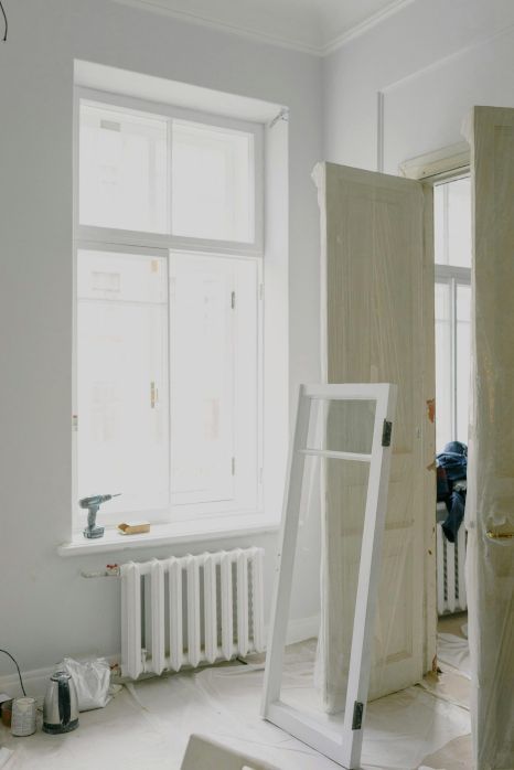 A room with a window and a door and a radiator being painted in white in Preston, UK.