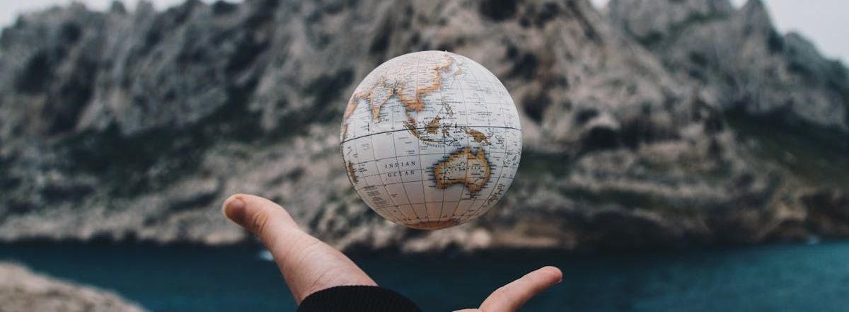 A person is holding a globe in their hands in front of a mountain.