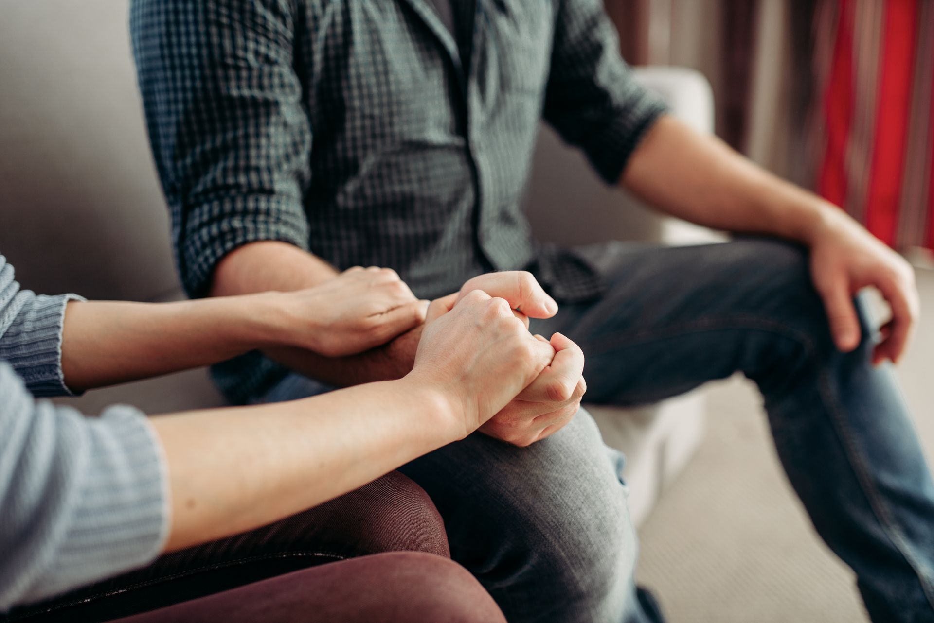Two people sitting together on a sofa, gently holding hands in a gesture of support or comfort. Two people sitting together on a sofa, gently holding hands in a gesture of support or comfort.