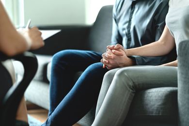A therapist takes notes while a couple sits on a couch together, holding hands during a counseling session.
