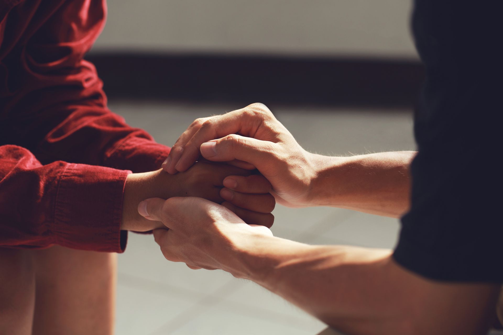 Two people holding hands, offering comfort or support against a neutral background. Two people holding hands, offering comfort or support against a neutral background.