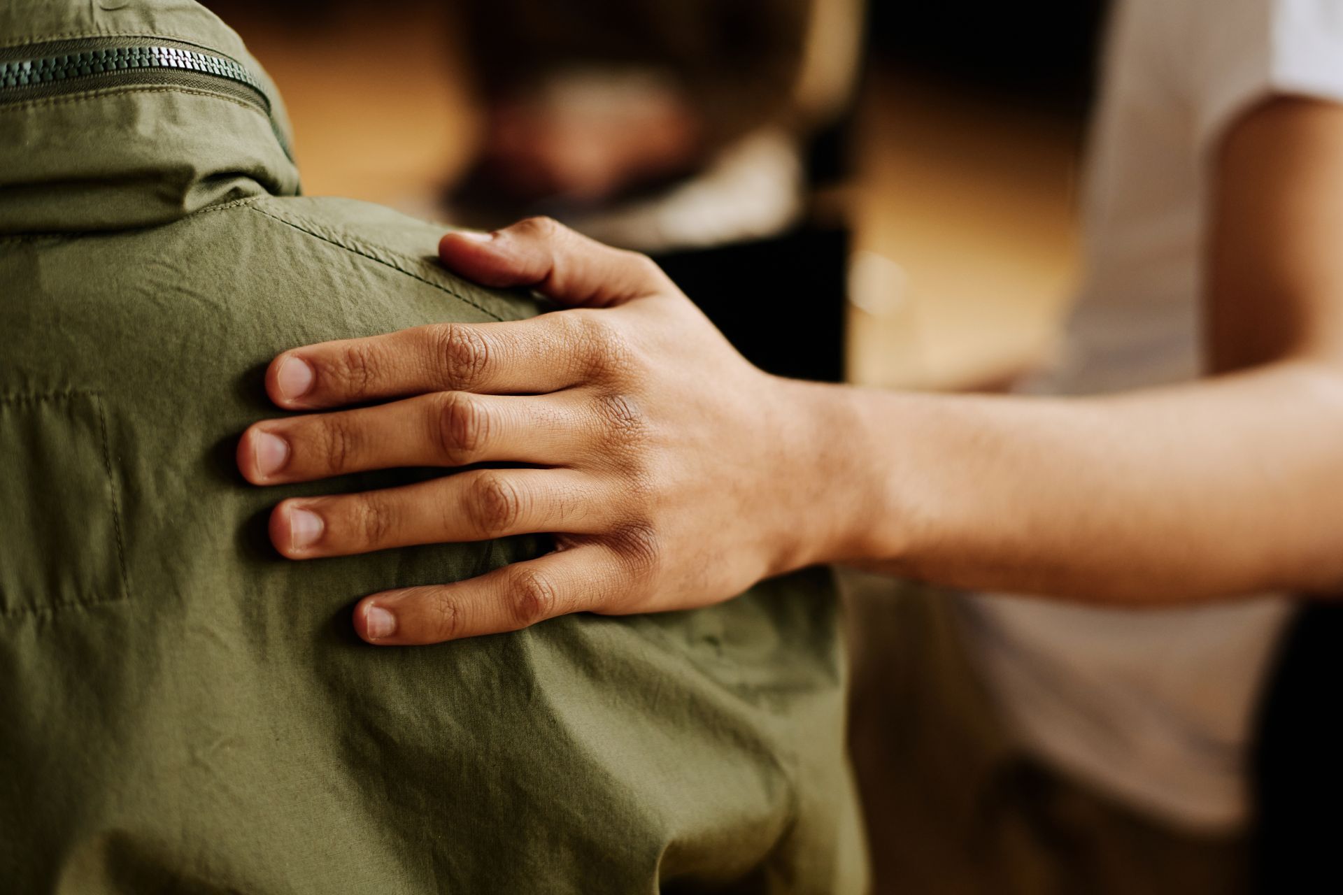 A hand rests supportively on the shoulder of a person wearing a green jacket, symbolizing comfort and reassurance.
