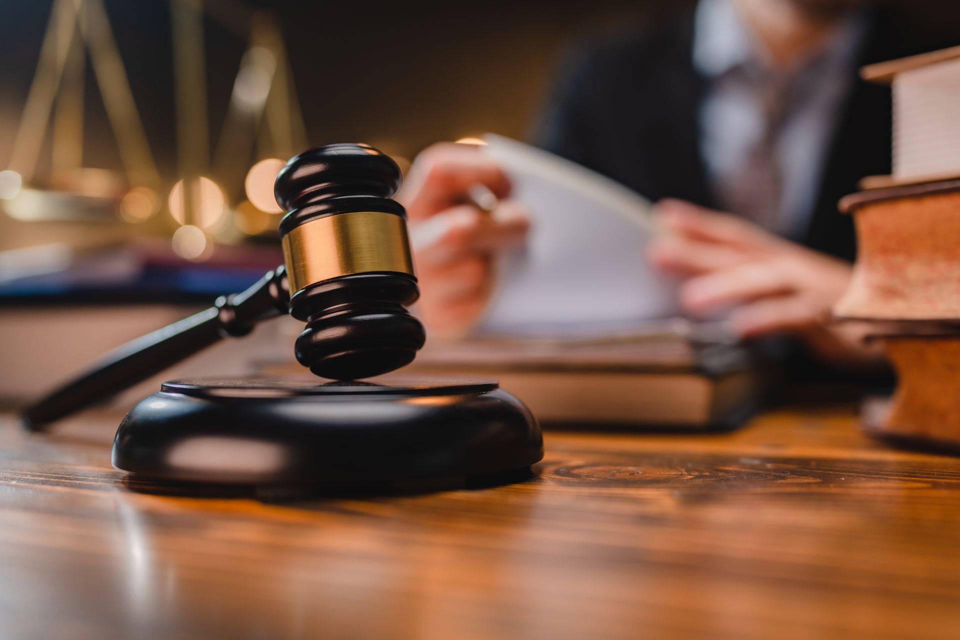 A wooden gavel rests on a desk in a law office with books and a scales of justice symbol in the background.