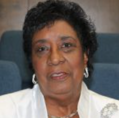 Woman with short dark hair wearing a white jacket, looking forward.