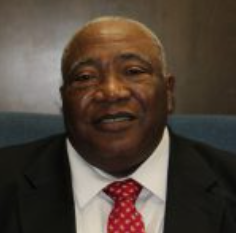Man in black suit and red tie, smiling indoors.
