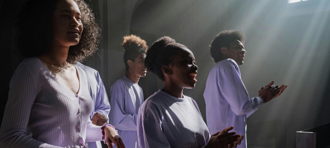 Four people in white clothing singing with sunlight streaming down.