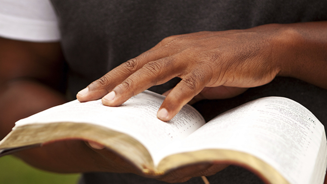 Person's hand on open book with yellowed pages.
