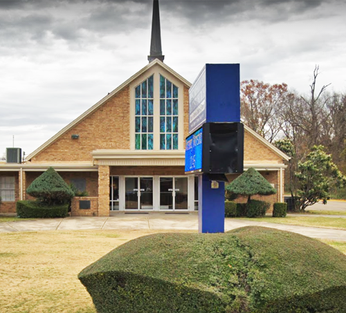 Church with a brick exterior, stained glass windows, and a blue electronic sign in front.