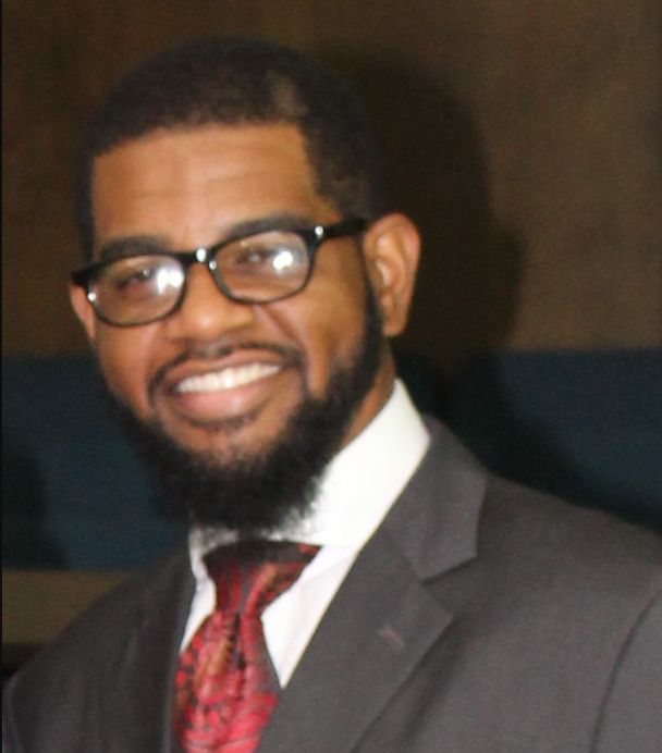 Man in suit and glasses smiles, indoors.