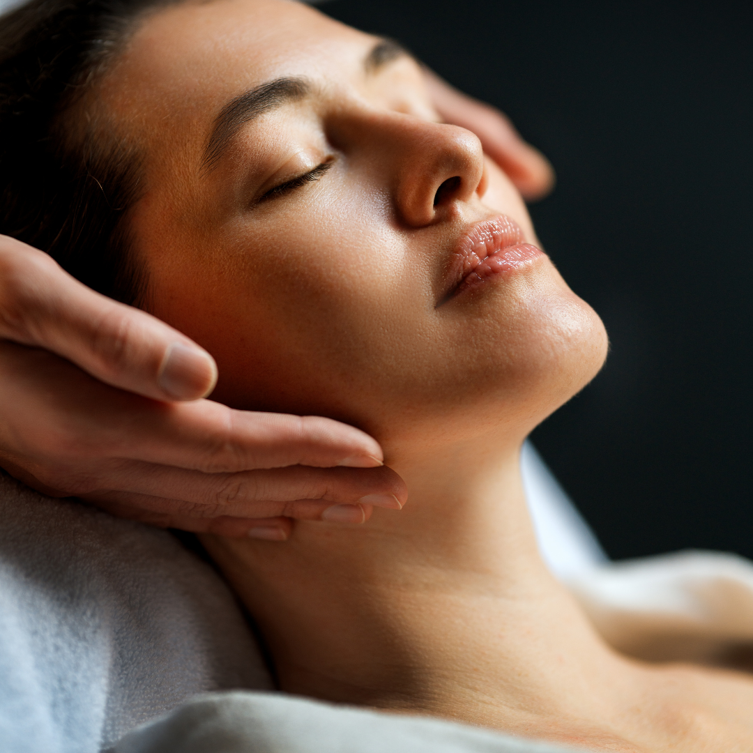 Woman with light skin, smiling, holding her cheeks, wrapped in a white towel, against a gray background.