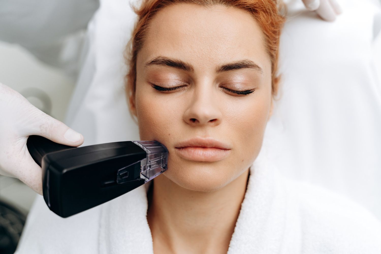 Woman lying with eyes closed during a facial treatment, with a handheld device near her cheek