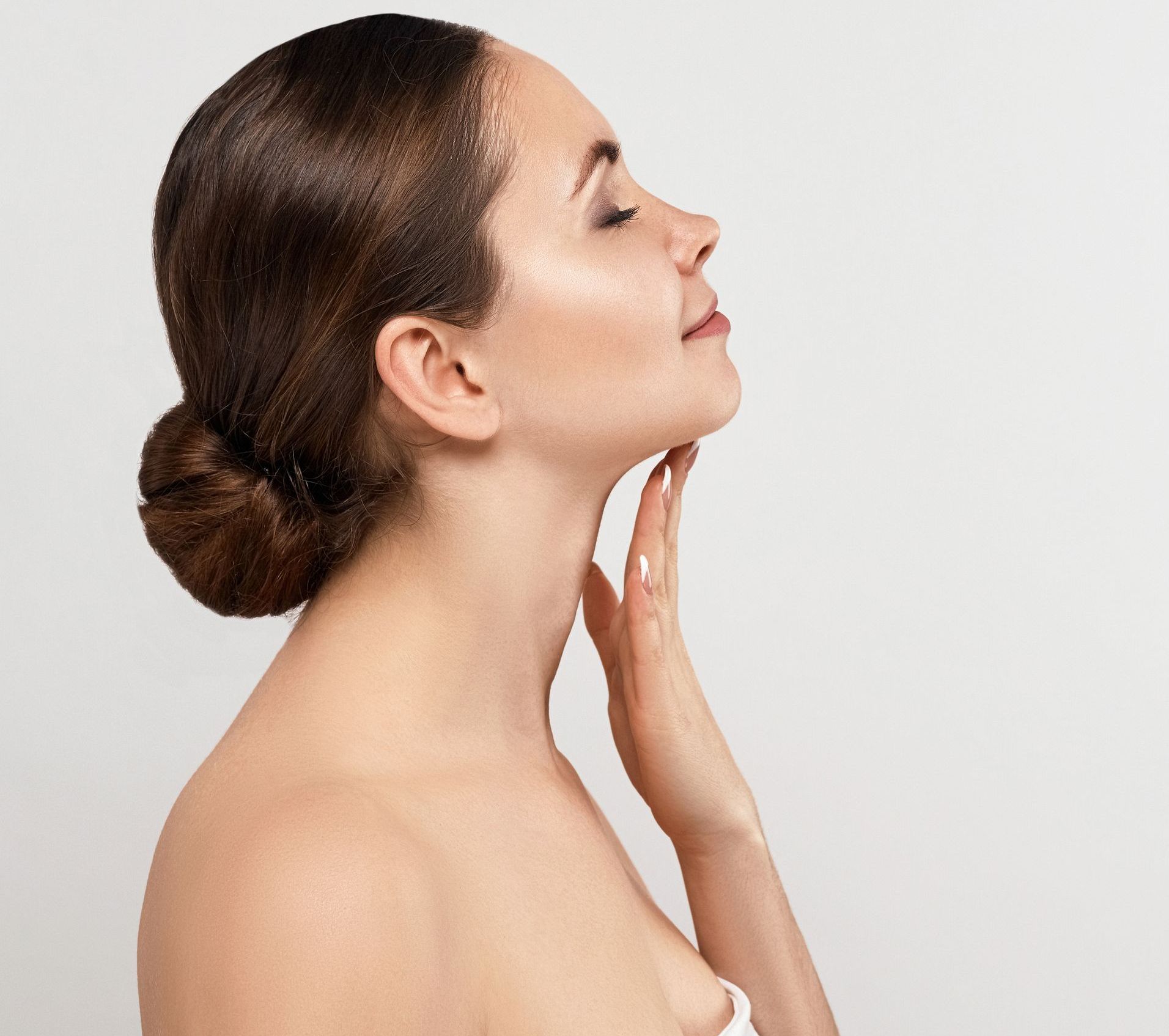 A woman is posing sideways and touching her neck