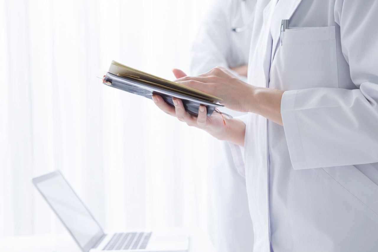 A doctor is holding a book in front of a laptop computer.