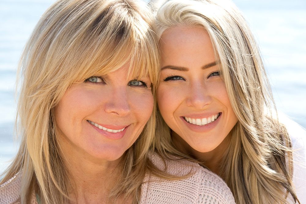 A mother and daughter are posing for a picture together and smiling.