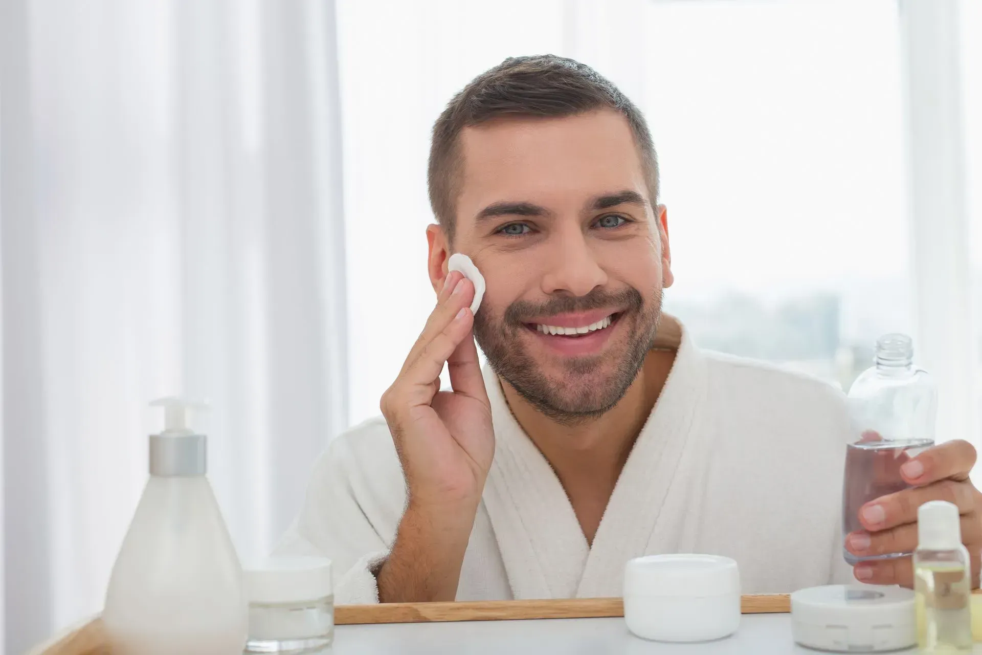 A man is smiling while cleaning his face with a cotton pad.
