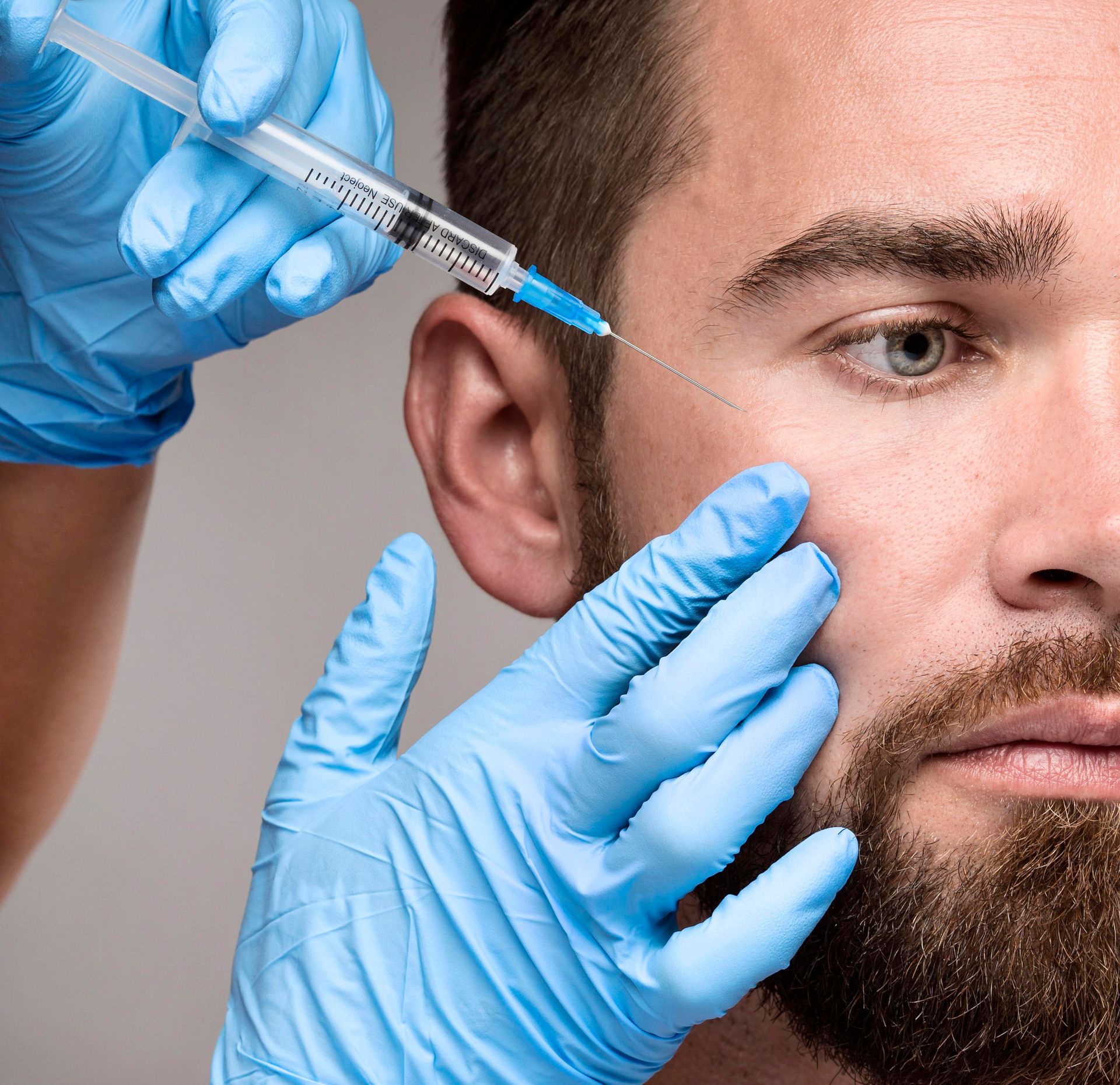 A man with a beard is getting a botox injection in his face.