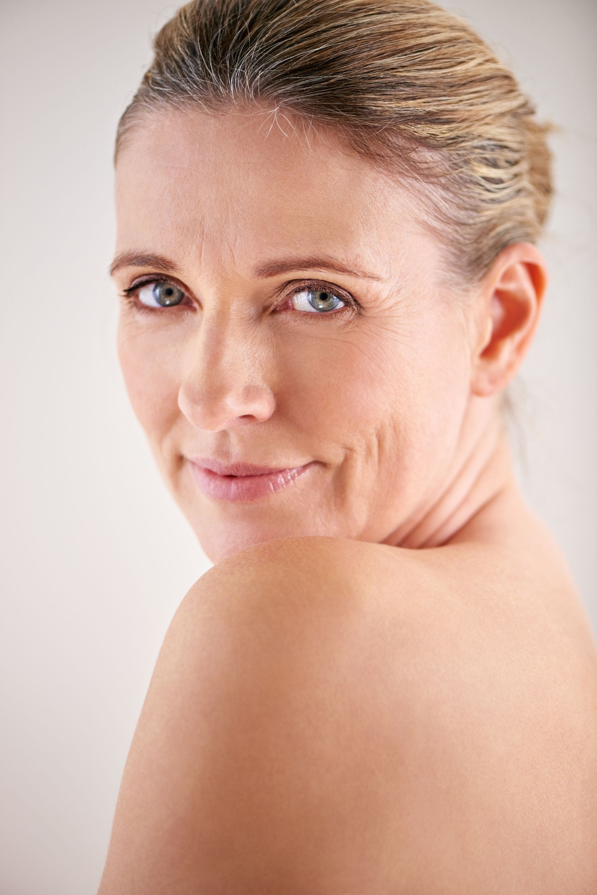 A woman without a shirt is smiling and looking over her shoulder at the camera.