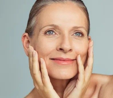A woman is touching her face with her hands and smiling.
