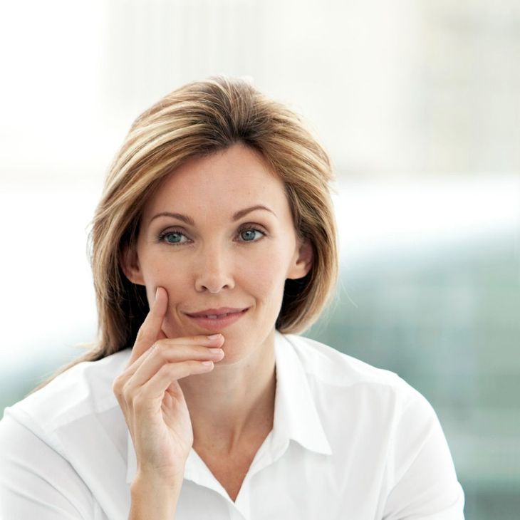 A woman in a white shirt has her hand on her chin